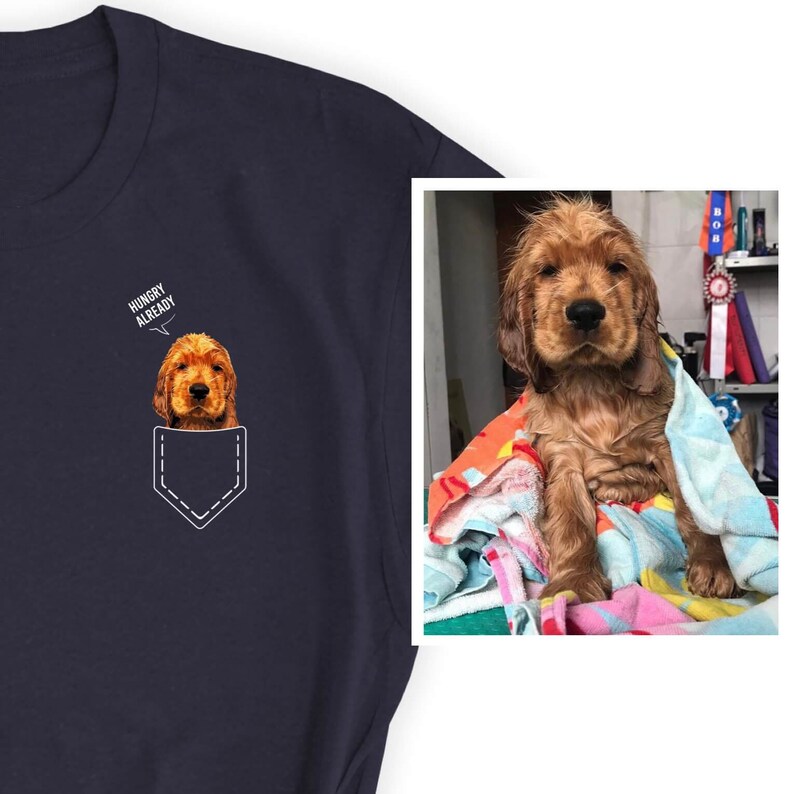 May include: Navy blue t-shirt featuring a graphic of a Cocker Spaniel puppy peeking out of a pocket, with the text "HUNGRY ALREADY" above it. The image also includes a photo of a wet Cocker Spaniel puppy wrapped in a towel.
