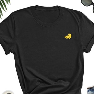 May include: A black t-shirt with a small yellow embroidered design of three bananas on the left chest.