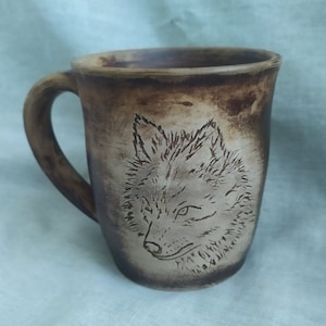 May include: A brown ceramic mug with a wolf design etched into the side. The wolf is facing the viewer and has a detailed, realistic look.