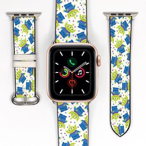 Può includere: Un Apple Watch color oro rosa con un cinturino bianco con un motivo ripetuto di alieni verdi in abiti blu. Il cinturino dell'orologio è mostrato in tre parti, con il quadrante che mostra le icone del telefono, della musica e della frequenza cardiaca.