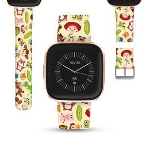 Puede incluir: Un smartwatch de color oro rosa con una esfera blanca y agujas negras. La esfera del reloj muestra la fecha "NOV 28" y la hora "96". El reloj tiene una correa amarilla y blanca con un patrón repetido de personajes de la franquicia de películas Toy Story.