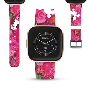 K&ouml;nnte beinhalten: Ein pinkfarbenes und wei&szlig;es Armband mit floralem Muster und einer wei&szlig;en Silhouette von Mickey Mouse und Minnie Mouse. Das Armband ist kompatibel mit einer Fitbit Versa Smartwatch in Ros&eacute;gold. Das Zifferblatt der Uhr zeigt das Datum "NOV 28" und die Zeit "96" an.
