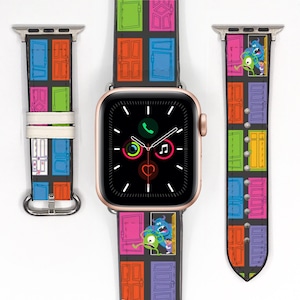 Puede incluir: Un Apple Watch negro con una banda colorida que presenta un patrón de puertas y personajes de la película Monsters Inc. La banda está hecha de cuero y tiene una hebilla de oro rosa.