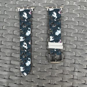 May include: Two watch straps with a dark teal background and a repeating pattern of white and black cartoon dragons and pink accents. The straps have silver-coloured hardware and a white leather strap.