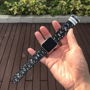 Może przedstawiać: Czarno-biały pasek do Apple Watch z wzorem Star Wars. Pasek ma biały pasek na górze i czarny skórzany pasek z białym nadrukiem postaci i statków kosmicznych z Gwiezdnych Wojen.