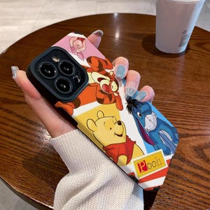 May include: A colorful phone case featuring Winnie the Pooh, Tigger, Piglet, and Eeyore. The case has a black camera lens cover and the text "Pooh" in red letters.