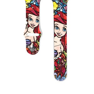 Peut inclure: Un bracelet coloré pour Apple Watch avec un motif de vitrail représentant Ariel de La Petite Sirène. Le bracelet est blanc avec des accents rouges, bleus, verts, jaunes et violets. Le motif comprend Ariel, Sébastien et Polochon.