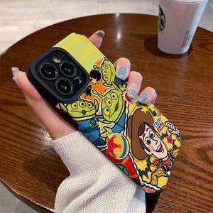 Puede incluir: Una funda de teléfono colorida con un diseño de dibujos animados con Woody de Toy Story y personajes de Alien de Toy Story. La funda tiene una cubierta de lente de cámara negra con tres lentes.