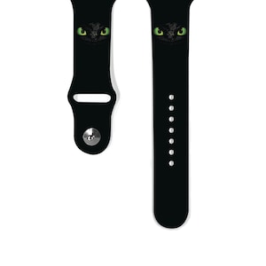 May include: Black silicone watch strap with a green eye graphic print. The strap is compatible with Apple Watch.