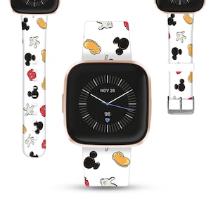 May include: A rose gold smartwatch with a white band featuring a pattern of Mickey Mouse gloves, ears, and shorts. The watch face displays the date, time, and a heart rate monitor. The band is secured with a silver buckle.