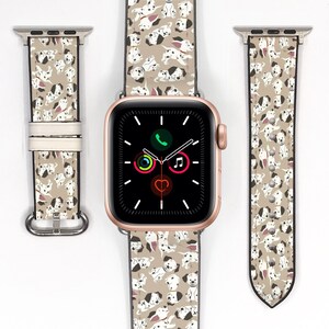 May include: A gold Apple Watch with a white band featuring a pattern of Dalmatian puppies. The watch face is black with white icons for phone, music, and a heart.