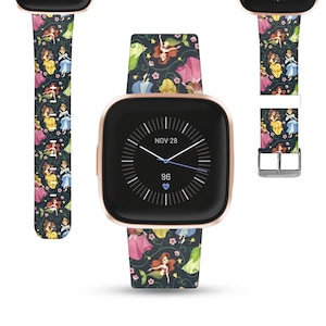 May include: A rose gold Fitbit Versa 3 smartwatch with a black watch face displaying the time "NOV 28" and "96". The watch has a colorful band with a repeating pattern of Disney princesses, including Ariel, Belle, Cinderella, and Snow White.