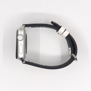 Op de afbeelding: Een zilveren Apple Watch met een zwart leren bandje. Het horloge gezicht is niet zichtbaar.