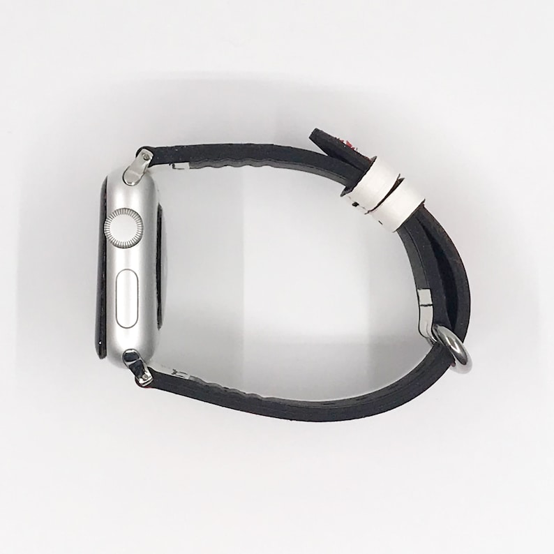 Op de afbeelding: Een zilveren Apple Watch met een zwart leren bandje. Het horloge gezicht is niet zichtbaar.
