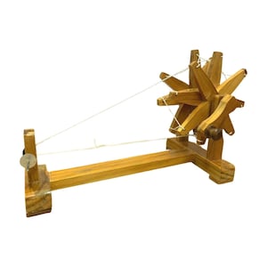 Side profile of a pale wood Gandhi charkha spinning wheel, shown as a portable hand spinning wheel for yarn.