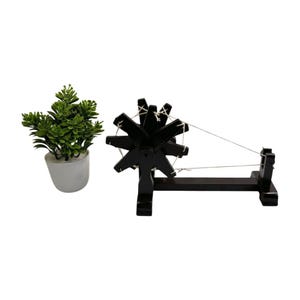 Mini scene with tiny plant, compact Gandhi charkha spinning wheel shown as portable tabletop piece.