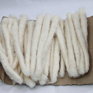 May include: A bundle of white cotton wicks, wrapped in brown paper. The wicks are long and thin, and they are arranged in a neat pile.