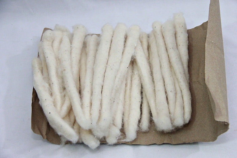 May include: A bundle of white cotton wicks, wrapped in brown paper. The wicks are long and thin, and they are arranged in a neat pile.