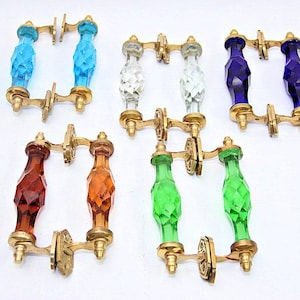 May include: Set of ten glass cabinet door pulls with brass hardware. The pulls are in various colours, including blue, green, amber, and clear. Each pull has a faceted design.