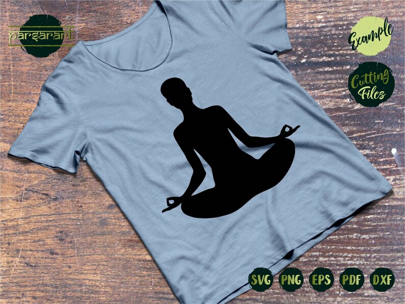 May include: A black silhouette of a person sitting in a yoga pose on a light blue t-shirt. The t-shirt is on a wooden surface. The text "Example Cutting Files" is in the upper right corner of the image.