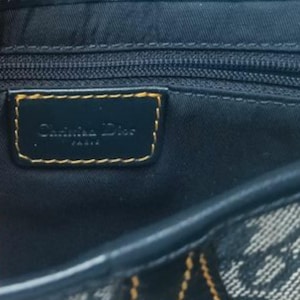 May include: Close-up of a navy blue handbag with a gold-trimmed label that reads "Christian Dior PARIS". The bag features a zipper and a patterned fabric design.