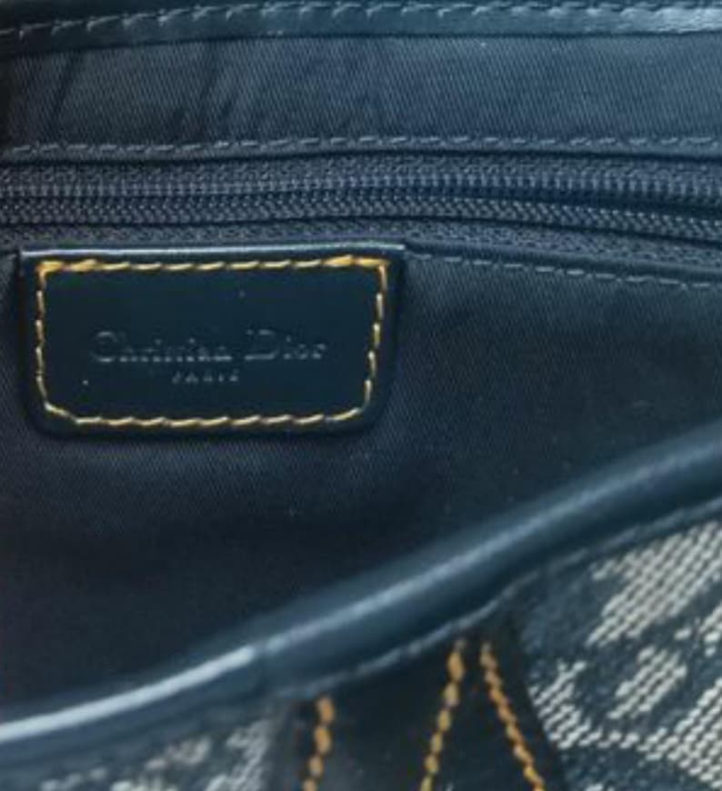 May include: Close-up of a navy blue handbag with a gold-trimmed label that reads "Christian Dior PARIS". The bag features a zipper and a patterned fabric design.