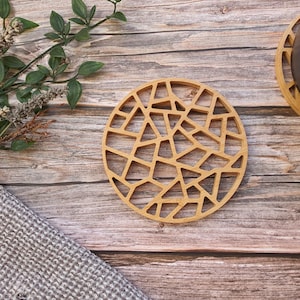 May include: A round wooden coaster with a geometric design. The coaster is made of light brown wood and has an intricate pattern of small triangles and squares.