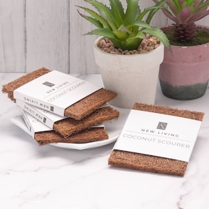 May include: A stack of four brown coconut scrubbers with a white label that reads "NEW LIVING COCONUT SCOURER".