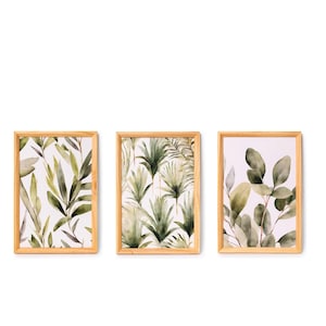 Pode incluir: Três impressões botânicas emolduradas com ilustrações em aquarela de folhas verdes e folhagens sobre um fundo branco. As molduras são feitas de madeira clara. As impressões são dispostas lado a lado.