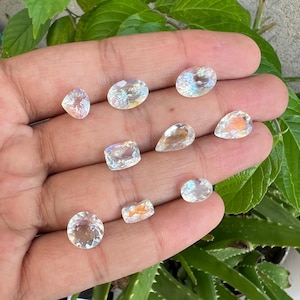 May include: Assortment of clear iridescent gemstones of various shapes and sizes, including oval, round, and pear shapes.