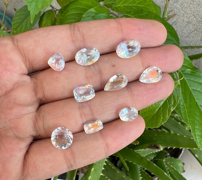 May include: Assortment of clear iridescent gemstones of various shapes and sizes, including oval, round, and pear shapes.