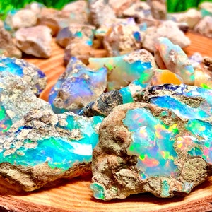 Może przedstawiać: Kolekcja surowych kamieni opalu z tęczowymi niebieskimi, zielonymi i żółtymi kolorami. Kamienie leżą na drewnianej powierzchni.