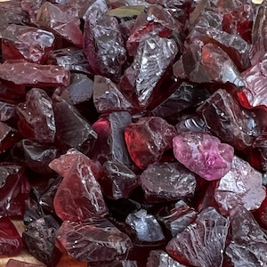 May include: A pile of deep red ruby gemstone chips. The chips are irregular in shape and have a translucent appearance.