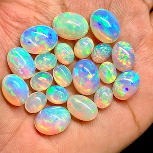 May include: A collection of oval-shaped opals in various sizes, displaying a rainbow of iridescent colors, including green, blue, and pink.