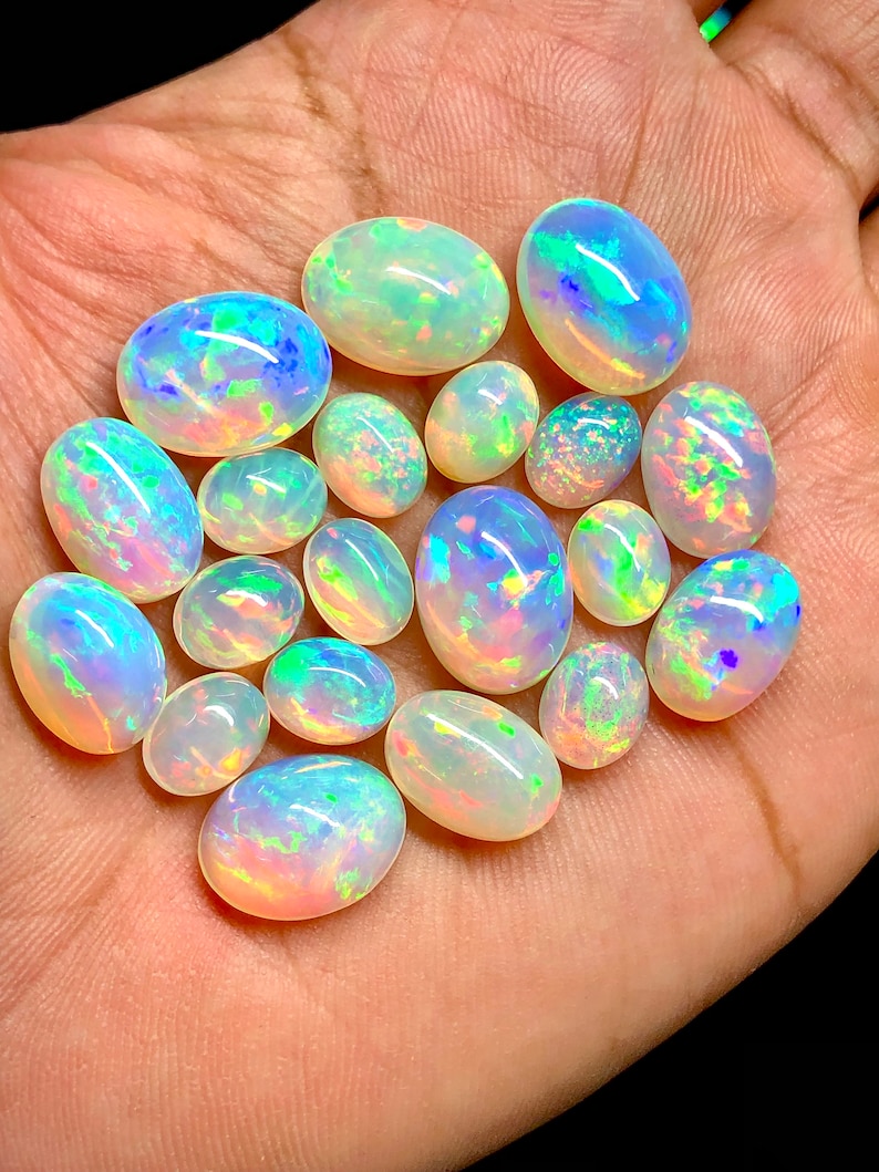 May include: A collection of oval-shaped opals in various sizes, displaying a rainbow of iridescent colors, including green, blue, and pink.