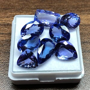 May include: A collection of eight blue pear-shaped gemstones in a white box. The gemstones are various shades of blue and have a smooth, polished finish.