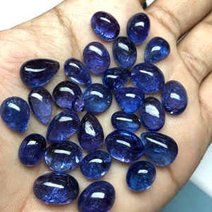 May include: A collection of polished, oval and teardrop-shaped blue gemstones. The gems vary in size and are displayed against a neutral background. The stones have a glossy finish, reflecting light, and are likely used for jewelry making or collecting.