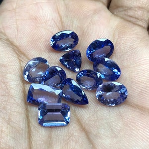 May include: A collection of ten faceted blue gemstones of various shapes and sizes. The gemstones are arranged on a hand.