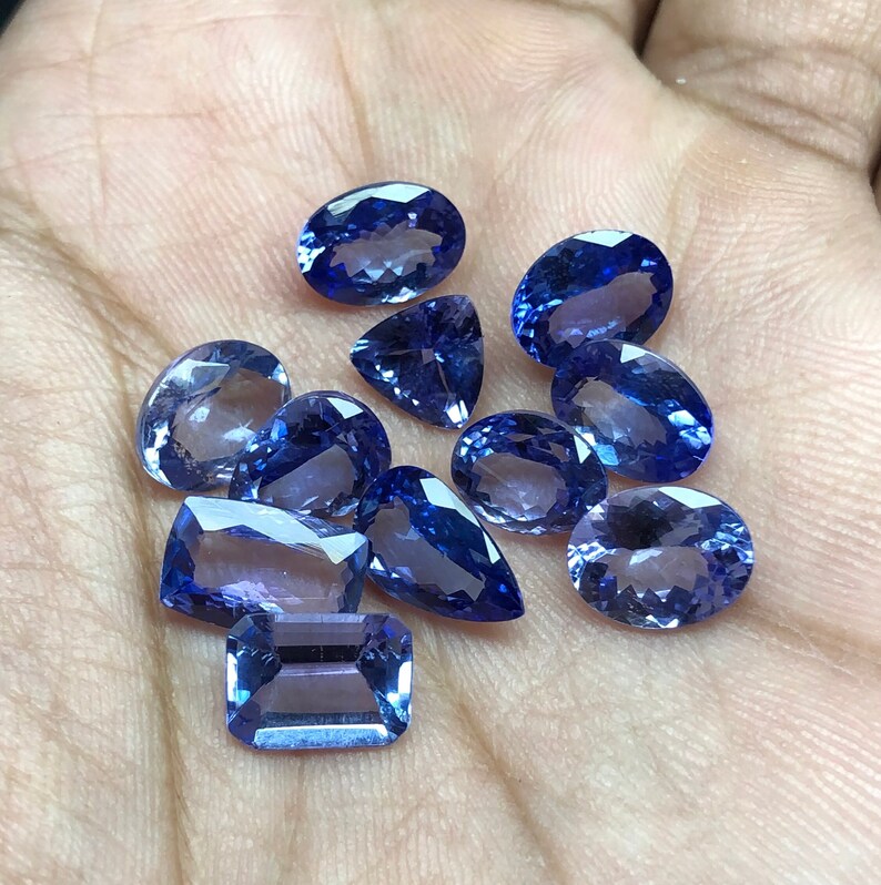 May include: A collection of ten faceted blue gemstones of various shapes and sizes. The gemstones are arranged on a hand.