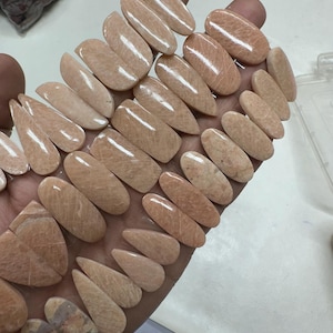 Coppia di pietre preziose cabochon color pesca abbinate, lotto all'ingrosso con forme e dimensioni diverse, utilizzate per la creazione di gioielli.