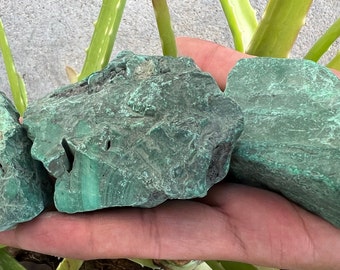 May include: Three rough, green malachite stones in various shapes and sizes. The stones have a natural, unpolished finish.