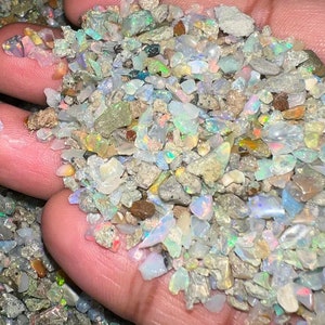 May include: A handful of small, iridescent opal chips in various shades of white, gray, and brown. The chips are mostly irregular in shape and have a slightly rough texture.