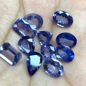 May include: A collection of ten faceted blue gemstones of various shapes and sizes. The gemstones are arranged on a hand.