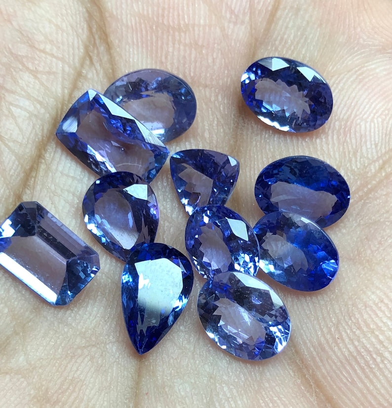 May include: A collection of ten faceted blue gemstones of various shapes and sizes. The gemstones are arranged on a hand.