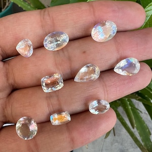 May include: A collection of nine iridescent moonstone gemstones in various shapes and sizes, including oval, pear, and square.