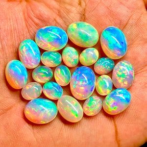 May include: A collection of 17 oval-shaped opal gemstones in various shades of white, blue, green, and pink. The opals are iridescent and have a rainbow-like sheen.