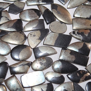 Pode incluir: Uma coleção de cabochões de pedras preciosas pretas e prateadas, com uma variedade de formas e tamanhos. As pedras têm um brilho metálico e são perfeitas para a fabricação de joias.