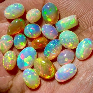 May include: A collection of 17 oval-shaped opals in various shades of white, yellow, and green. The opals are iridescent and have a rainbow-like sheen.