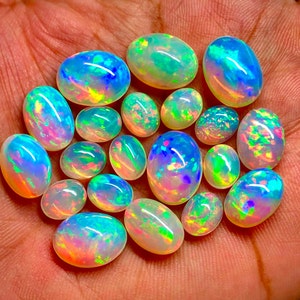 May include: A collection of 17 oval-shaped opals in various shades of white, blue, green, and pink. The opals are iridescent and have a rainbow-like sheen.