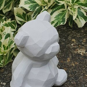 K&ouml;nnte beinhalten: Eine wei&szlig;e, geometrisch geformte Teddyb&auml;r-Figur. Der B&auml;r sitzt mit gekreuzten Beinen und hat ein schlichtes, modernes Design.